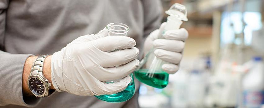 Hands with gloves holding two beakers.